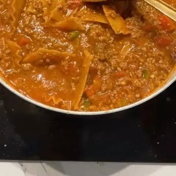 A pot of beef and wide pasta simmering in tomato sauce with peppers.